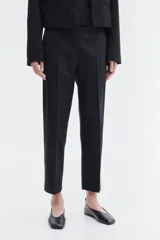 Pantalón cigarette tobillero negro con cintura estándar, cierre y pretina prolongada con corchete oculto. Piernas ajustadas con abertura corta en los bajos, bolsillos al bies y bolsillo de atrás decorativo. Pliegues adelante y atrás.