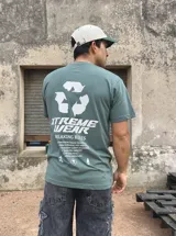 Remera verde oliva de algodón con estampado en la espalda que incluye un símbolo de reciclaje, el logo de la marca Xtreme Wear, la frase 'Breaking Rules' y un texto con tipografía pequeña.