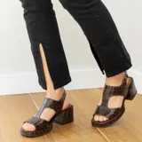 Sandalias de cuero vacuno color marrón con textura tipo cocodrilo, taco ancho y plataforma. Diseño con puntera descubierta y tira ancha sobre el empeine con aberturas laterales. Cierre con hebilla en el tobillo.