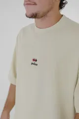 Remera color beige de corte holgado, con cuello redondo y mangas cortas. Estampado pequeño en el pecho con el logo de la marca Pulau.