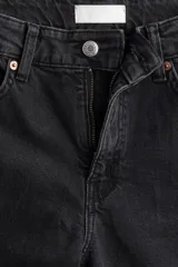 Pantalón de jean negro de corte ancho, largo tobillero y terminación desflecada. Con tiro alto, cinco bolsillos, cierre con cremallera y botón metálico.