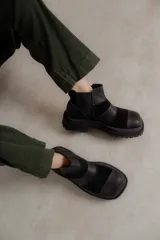 Bota de cuero negra con punta cuadrada y paneles de cuero liso y gamuza. Tiene elásticos laterales, suela track y tirador trasero.