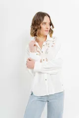 Camisa blanca de voile con bordados calados en el frente, cuello camisero, mangas largas con puños abotonados y cierre frontal con botones. 