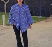 Camisa celeste con estampado floral blanco, cuello clásico, cierre con botones y mangas largas abullonadas con puños elásticos.