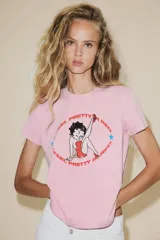 Camiseta rosa de manga corta y cuello redondo con estampado de Betty Boop y texto "I feel pretty in red". Debido al proceso de tintado y lavado, el color de cada prenda es único y especial por lo que puede presentar diferencias con respecto al mostrado en la foto.