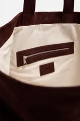 Bolso tipo shopper marrón de piel con acabado serraje. Tiene dos asas de mano y un bolsillo interior con cierre.