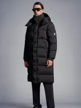 Campera larga negra con capucha desmontable y cierre frontal.
