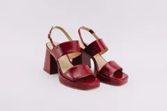 Sandalias de plataforma color borgoña, confeccionadas en charol. Tienen dos tiras anchas sobre el empeine, pulsera con hebilla al tobillo y taco cuadrado de 9 cm.
