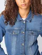 Chaqueta de jean azul con cuello clásico, cierre frontal con botones metálicos, bolsillos con solapa abotonada en el pecho y corte regular.