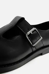 Zapato tipo Mary Jane de cuero negro con hebilla lateral, horma redonda y suela con ligero tacón.