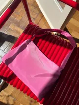 Cartera de lona semi impermeable color lila, con cierre metálico, forrería de gross y bolsillo interno. Tiene tira regulable para usar colgada al hombro, cruzada o como riñonera.
