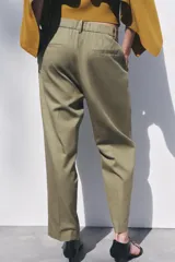 Pantalón color verde oliva de tiro medio con cintura con trabillas, bolsillos laterales, pinzas delanteras y raya planchada. Cierre frontal con cremallera, botón y ganchos metálicos.