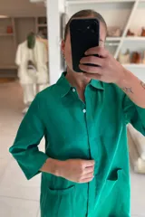 Vestido camisero color celeste de lino, con cuello clásico, cierre frontal con botones y mangas 3/4. Tiene dos bolsillos de parche en el pecho y corte irregular en el ruedo.