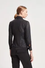 Camisa negra de punto con rayas verticales en lurex, calce slim, cuello alargado, apertura en cartera delantera, botones negros y pinzas traseras.