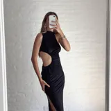 Vestido largo negro con cuello alto, sin mangas y abertura en la cintura.