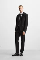 Blazer slim fit negra confeccionada en tejido con viscosa. Cuello con solapas de muesca, manga larga con puño con detalle de botones, bolsillo de vivo en pecho y de solapa en cadera, bolsillo interior, bajo con aberturas en espalda y cierre frontal con botones.
