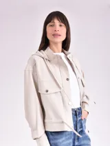 Chaqueta color crudo con capucha, cierre con botones a presión, bolsillos delanteros con solapa y cordón ajustable en la cintura.