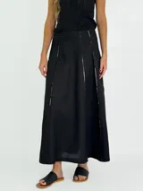 Pollera larga negra de corte amplio, con costuras verticales que simulan pliegues y terminaciones deshilachadas. Se combina con una musculosa negra de escote redondeado.