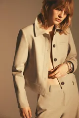Chaqueta color beige de cuello solapa y manga larga con hombreras acabada en puño. Presenta bolsillos laterales y falso bolsillo de vivo en pecho. Cierre frontal con botones.
