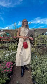 Bandolera pequeña tipo 'phone bag' de símil cuero color rosado pálido, con cierre de cremallera y correa ancha de tela con diseño de chevron en tonos claros.