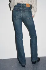 Pantalón de jean azul oscuro, de tiro bajo, corte slim fit y bootcut. Con cinco bolsillos y cierre frontal con cremallera y botón.