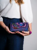 Billetera de tela bordada con diseño de pájaro en tonos violeta, azul y verde. Cuenta con cierre de cremallera y tirador con pompón y cuentas de madera.