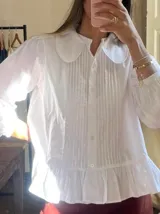 Camisa blanca con cuello bebé, mangas largas abullonadas y pechera con tablillas verticales.