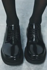 Zapato tipo mocasín negro acharolado con punta redonda y cierre de cordones. Suela de 4 cm de altura.