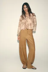 Camisa con estampado animal print en tonos beige y marrón, con cuello solapa y escote pico. Manga larga con capas en mismo tejido y bajo acabado en volantes. Cierre frontal con botones y lazada.