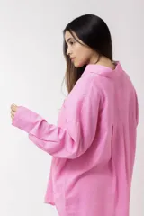 Camisa blanca de lino, de corte holgado, con cuello clásico, cierre frontal con botones, bolsillo en el pecho y mangas largas con puños abotonados.