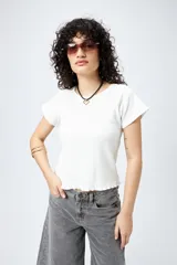 Remera blanca de punto acanalado con silueta relajada, manga corta raglán y ruedo ondulado.