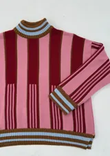 Sweater de punto oversize a rayas verticales rosas y bordó, con cuello alto y puños con ribete celeste.