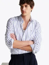 Camisa de popelín de puro algodón a rayas verticales blancas y celestes con logo de Tommy Hilfiger bordado en el pecho. Cuenta con cuello abotonado, mangas largas con puños abotonados y corte regular.