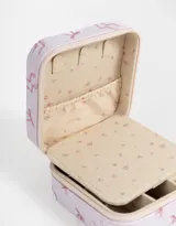 Caja cuadrada porta bijou color lila con estampado de moños rosas y cierre perimetral con cremallera.