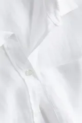 Camisa blanca de lino con cuello clásico, abotonada al frente, de manga larga con puños abotonados, canesú en la espalda, bolsillo de parche en el pecho y bajo redondeado.