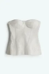 Top bustier color crudo de sarga con escote strapless, copas acolchadas y costuras decorativas adelante y atrás. Varillas adelante para dar forma y aportar sujeción, y cierre visible en la espalda.