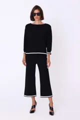 Conjunto de pantalón y sweater color crema con ribetes negros. El sweater es de corte recto con cuello redondo y mangas 3/4. El pantalón es palazzo con ribete negro en el ruedo.
