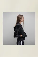 Campera de terciopelo negro brilloso con capucha, cierre frontal, bolsillos laterales, puños y cintura ajustados. Silueta relajada.