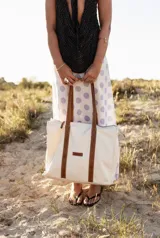 Bolso tipo tote color crudo con asas de cuero marrón.