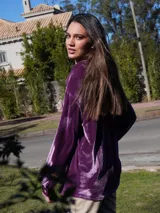 Camisa roja de terciopelo con cuello clásico, botones frontales y mangas largas con puños abotonados. Tiene dos bolsillos de parche en el pecho.