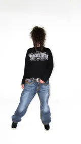 Remera negra oversize de manga larga, confeccionada en jersey de algodón grueso. Presenta cuello ancho y estampado frontal con el logo de la colaboración LUCCABOSSIO x Saint.