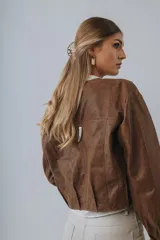Campera bomber marrón de cuero con cierre frontal y broche plateado decorativo en la espalda.