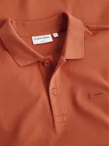Chomba color ladrillo de corte slim, con cuello clásico, tapeta de dos botones, mangas cortas y logo bordado en el pecho.
