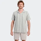 Camisa de manga corta con cuello cubano, color gris claro con rayas verticales en blanco y gris más oscuro. Presenta un bolsillo en el pecho y cierre frontal de botones.