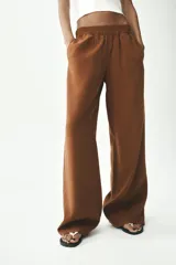 Pantalón marrón de tiro alto con cintura elástica, bolsillos delanteros y detalle de banda lateral blanca a contraste.