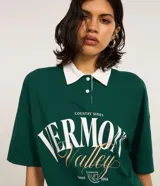 Camisa polo verde oscuro de algodón con cuello blanco contrastante, cierre de botones y mangas cortas. Estampa frontal con lettering "Vermont Valley".
