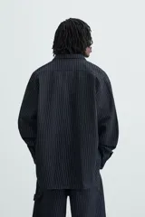 Camisa negra con finas rayas verticales blancas, de corte holgado, manga larga y cuello abotonado.