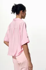 Camisa cropped color rosa de lino, con cuello solapa, escote pico, manga corta y bolsillos delanteros de plastrón.