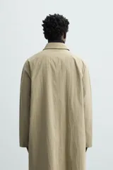 Gabardina color arena de corte amplio, con cuello solapa, manga larga, cierre frontal con botones y bolsillos laterales con solapa.