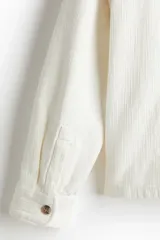 Sobrecamisa color crema en tejido texturizado de algodón, corte estándar, con cuello inglés, tapeta lisa, bolsillos superiores abiertos, canesú en la espalda, mangas largas con puños abotonados y bajo recto.